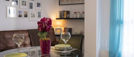 A dining area with a glass table, two wine glasses, a vase with flowers, and a brown leather couch.