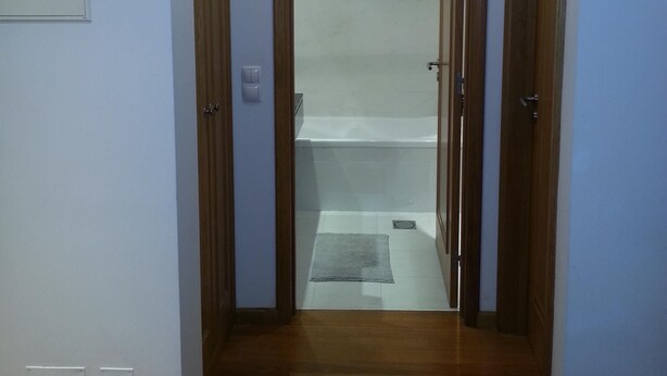 Un pasillo con piso de madera que conduce a un baño con bañera y ducha.