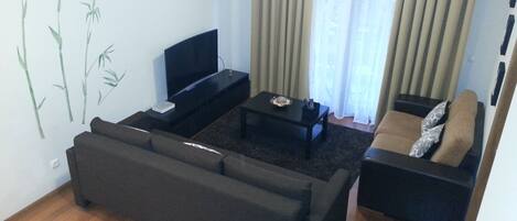 A living room with a sofa, a coffee table, a TV, and a wall with bamboo artwork.