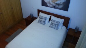 Una cama bien hecha con dos almohadas, una mesita de noche con una lámpara y un cuadro de una flor colgado en la pared.