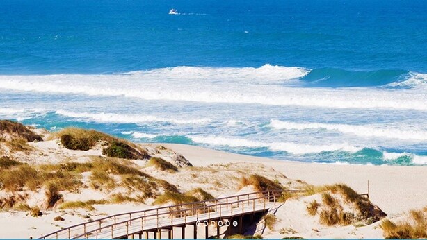 A beach with a wooden pier leading to a boat. - Apartment in Praia D'El Rey Golf & Beach Resort (Amoreira)