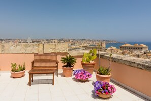 A rooftop terrace with a wooden bench, potted plants, and a view of the cityscape and sea. - The Myth. Central in Ortigia. Kid-friendly (Siracusa)