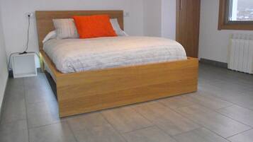 Un dormitorio moderno con estructura de cama de madera, colchón blanco y almohada naranja.