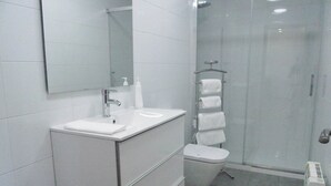 Uma casa de banho moderna com lavatório, espelho e sanita brancos.