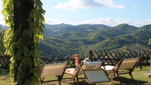 A view of a mountainous landscape with a wooden fence and two lounge chairs facing the scenery.