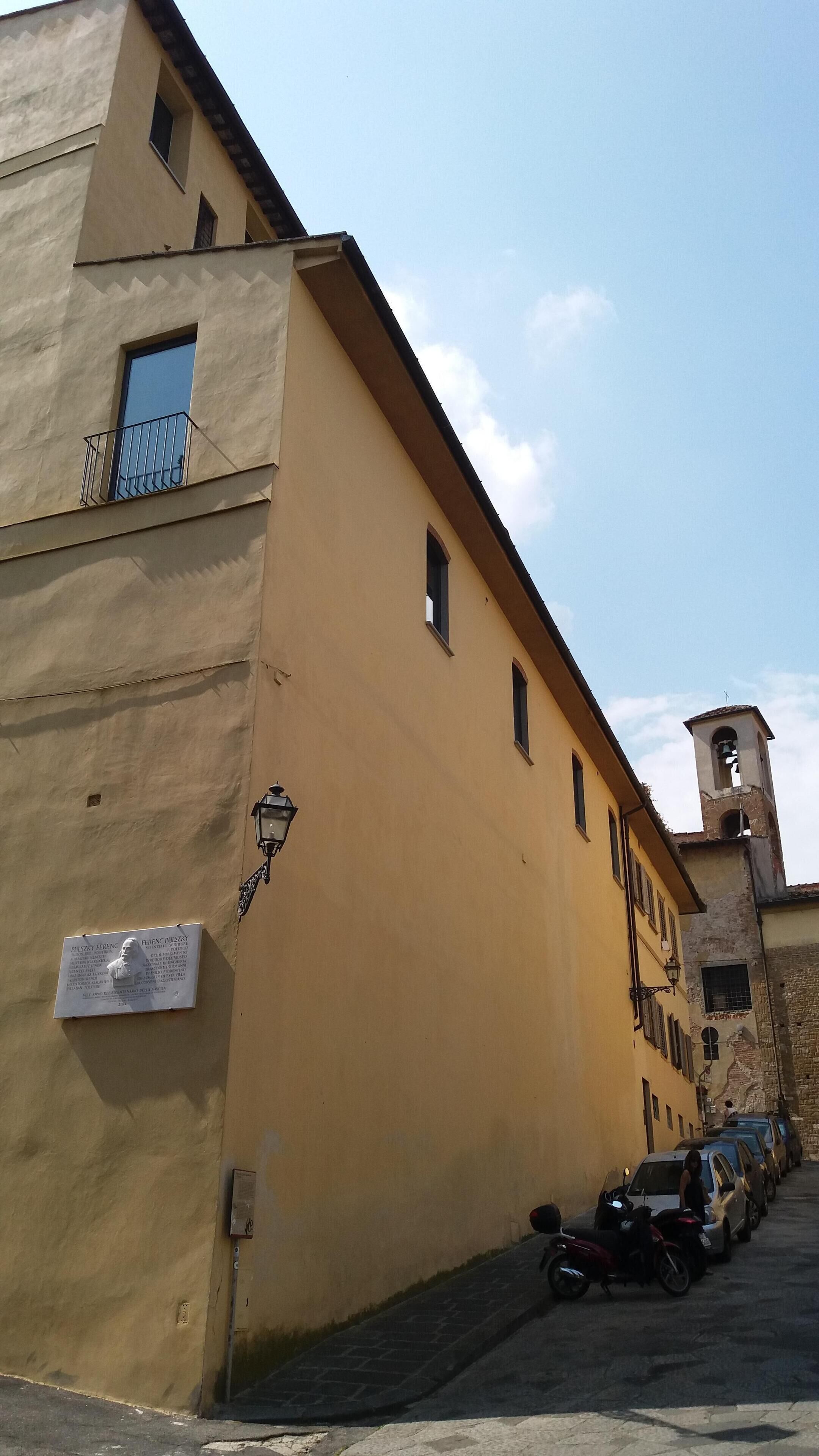 A yellow building with a small balcony, a bell tower, and a plaque on the wall.