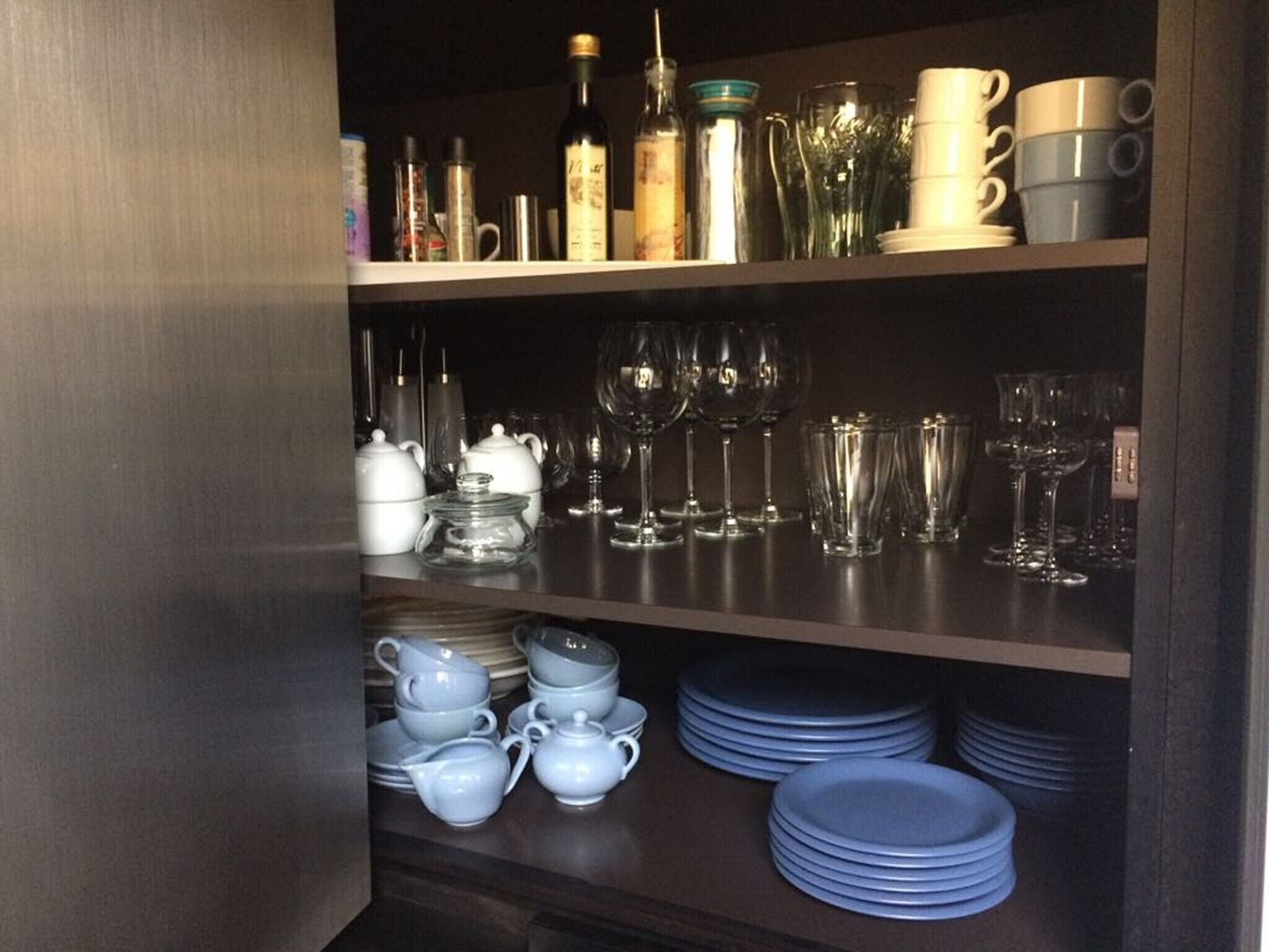 Un meuble de cuisine doté d’étagères où sont rangés différents types de verrerie, notamment des verres à vin, des verres à cocktail et des bols.