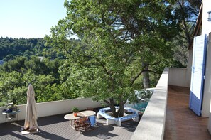 A rooftop terrace with a table, chairs, a potted plant, and a blue awning.