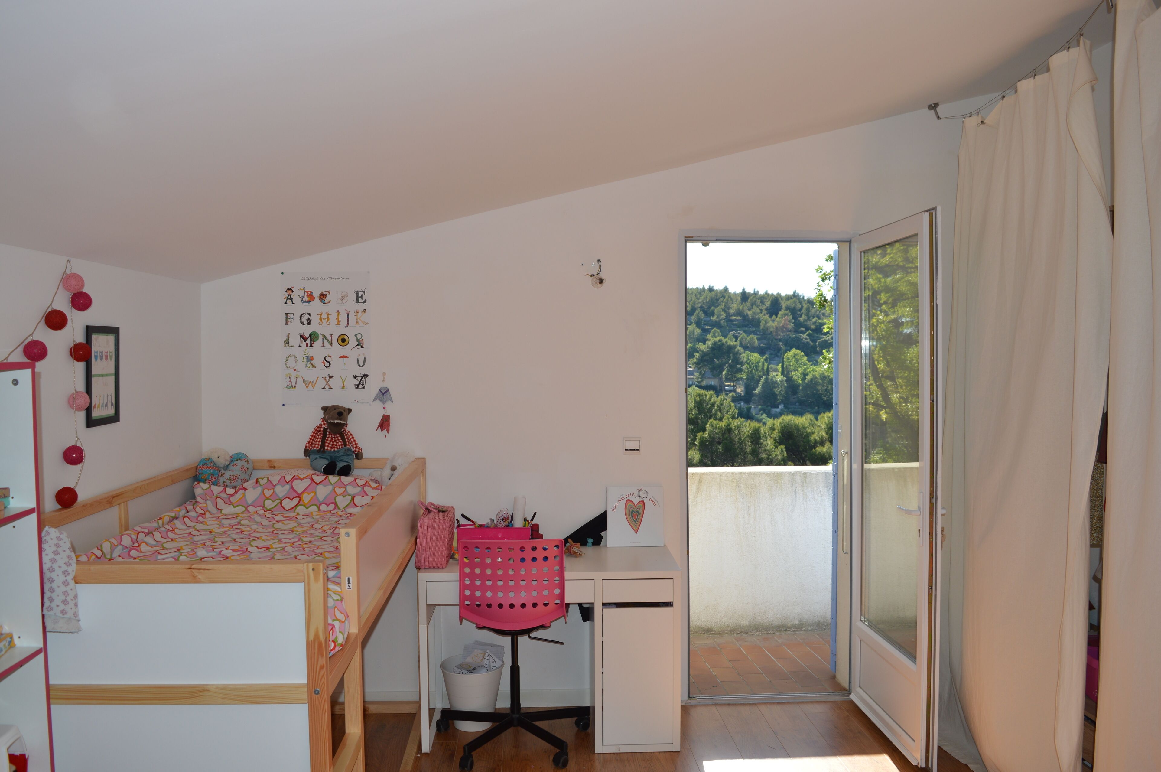 A child's bedroom with a bed, desk, and a view of a forest through a sliding door.