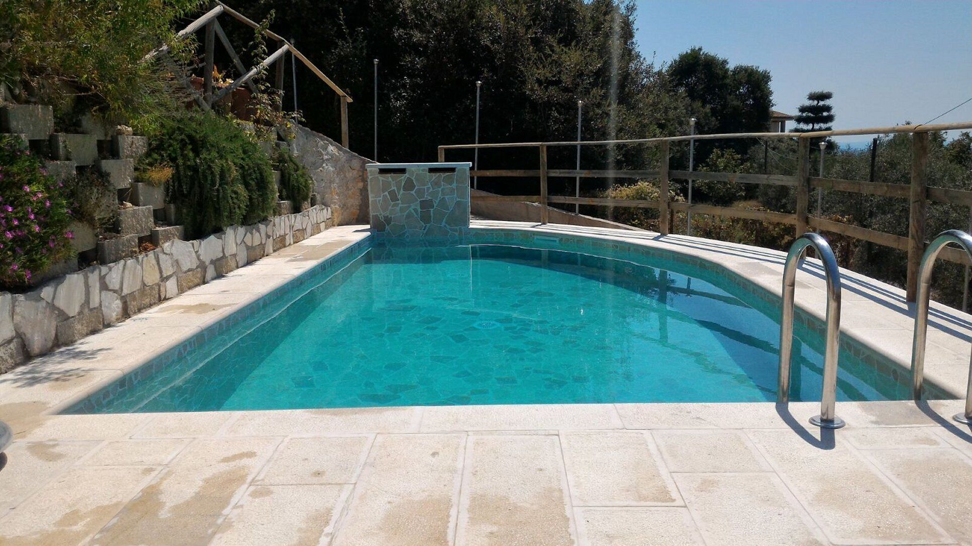 A swimming pool with a stone wall and metal railing.