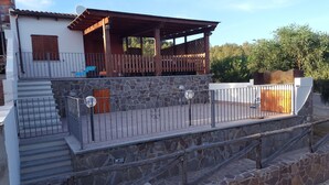 A two-story building with a stone facade, a wooden deck, and a metal railing. - Chalet in Sardinia (Villaputzu)