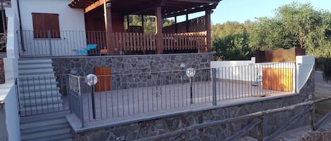 Un edificio de dos pisos con fachada de piedra, una terraza de madera y una barandilla de metal.