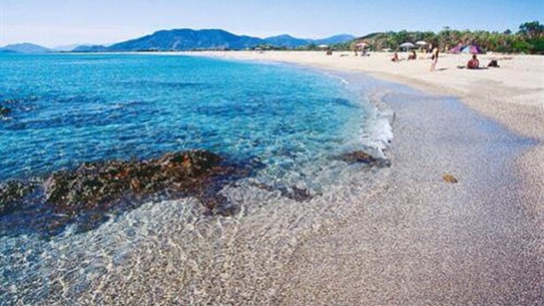 A beach with clear water, pebbly shore, and distant mountains. - Chalet in Sardinia (Villaputzu)