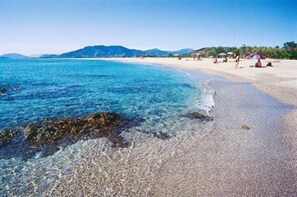 A beach with clear water, pebbly shore, and distant mountains. - Chalet in Sardinia (Villaputzu)