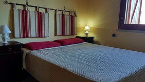 A hotel room with a bed, two nightstands, a lamp, and a window with blinds. - Chalet in Sardinia (Villaputzu)
