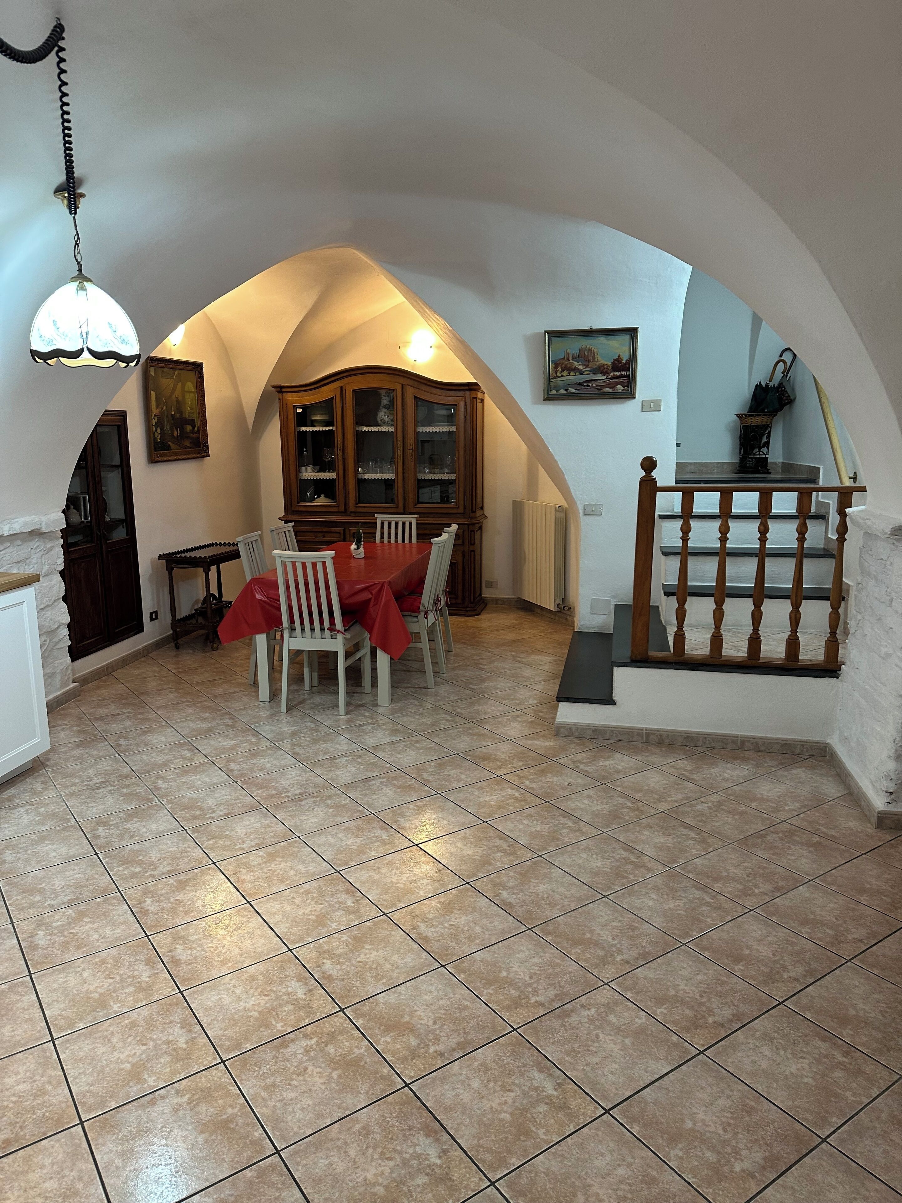 A dining area with a red tablecloth, white chairs, and a wooden cabinet.