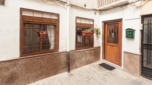 A narrow alleyway with two windows, one with a wooden shutter and the other with a metal grid. There is a door with a wooden panel and a green mailbox on the wall. - LOFT UNDER HOUSING CENTER OF VALENCIA- CIUTAT VELLA (València)