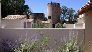 A courtyard with a tower, surrounded by buildings with tiled roofs and a variety of plants.