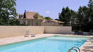 A rectangular swimming pool with a metal ladder, two lounge chairs, and a beige wall.