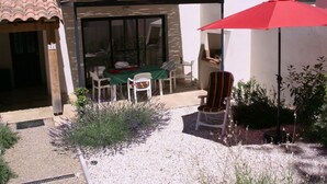 A patio area with a table and chairs, a red umbrella, and a small garden with lavender plants.