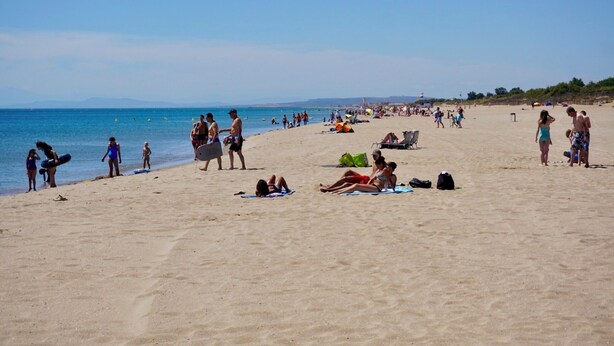 A crowded beach with people sunbathing and swimming.