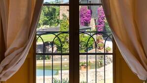 A bed with neatly folded towels, a view of a garden with a stone bridge, and a building with pink flowering trees.