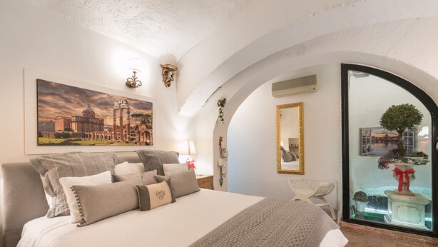 A bedroom with a large bed, a painting of a historical building, a mirror, and a view of a fountain through a glass door. - Luxury Holiday House Luxury Holiday House CIN: IT058091B4O8TGUF2I (Roma)