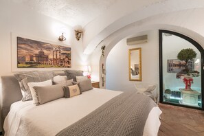 Een slaapkamer met een groot bed, een schilderij van een historisch gebouw, een spiegel en uitzicht op een fontein door een glazen deur.