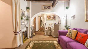 A cozy living room with a purple sofa, a fireplace, and a dining area with a table set for two. - Luxury Holiday House Luxury Holiday House CIN: IT058091B4O8TGUF2I (Roma)