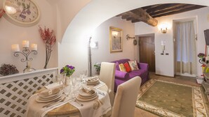 A dining area with a round table set for four, a clock on the wall, and a purple sofa in the background. - Luxury Holiday House Luxury Holiday House CIN: IT058091B4O8TGUF2I (Roma)