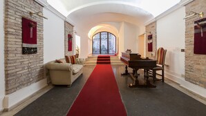 A grand hallway with a red carpet leading to a piano and a sofa, flanked by brick walls and a large arched window. - Luxury Holiday House Luxury Holiday House CIN: IT058091B4O8TGUF2I (Roma)