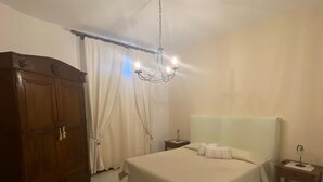 Un dormitorio con una cama grande, un armario de madera, una mesita de noche, una silla y una araña.