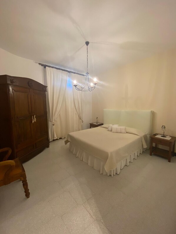 Un dormitorio con una cama grande, un armario de madera, una mesita de noche, una silla y una araña.