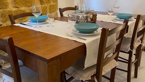 Una mesa de comedor de madera dispuesta con platos azules y copas de vino, rodeada de sillas con manteles blancos.