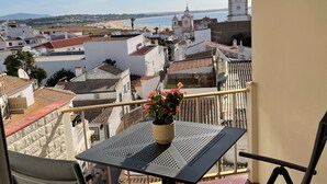 Un balcó amb taula i cadires, que domina una ciutat costanera amb edificis i una torre de l'església.