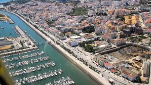 Vista aèria d'una ciutat costanera amb un port esportiu ple de vaixells, edificis urbans densos i una vista clara de la mar.