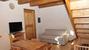 Un salon chaleureux avec une table à manger en bois, un canapé, un téléviseur posé sur un meuble et un escalier en bois.