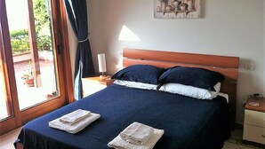 Un dormitorio con cama, mesita de noche, lámpara y ventana con cortinas.