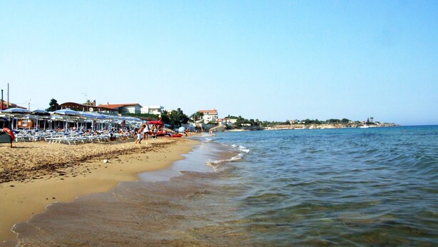 A beach with sun loungers and umbrellas, a sandy shore, and buildings in the background. - Smell of sea house (Avola)