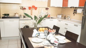 A modern kitchen with white cabinets, a dining table set with plates, cups, and a fruit bowl. - Smell of sea house (Avola)