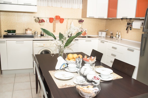 A modern kitchen with white cabinets, a dining table set with plates, cups, and a fruit bowl.