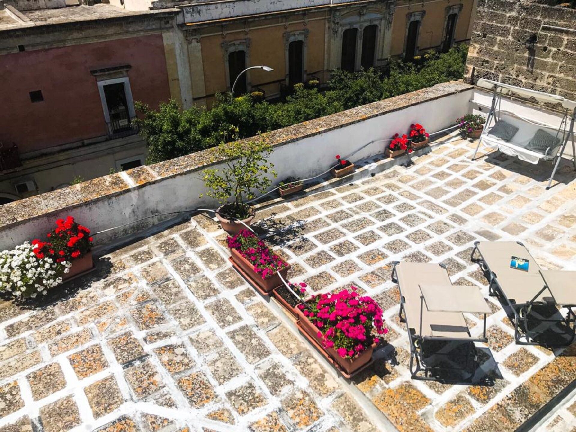 Terraço no telhado com piso de azulejos, plantas em vasos e mobiliário de exterior.