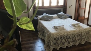 Ein ordentlich gemachtes Bett mit Sprenkeldecke, eine Nachttischlampe und ein Fenster mit Jalousien.