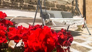 Eine Liege mit Baldachin, eine Steinmauer und im Vordergrund rote Blumen.