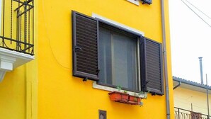 Een gebouw met twee verdiepingen, een gele gevel, een houten deur en een klein balkon met een metalen hekwerk.