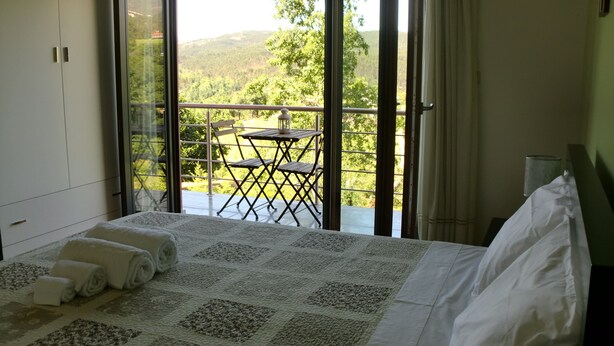 A bedroom with a bed, a view of a balcony with a table and chairs, and a window with curtains.