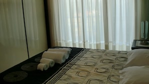 A hotel room with a bed, a nightstand, and a window with sheer curtains.