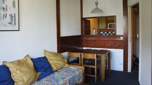 Un espace de vie compact comprenant un canapé, une table à manger et un coin cuisine visible à travers une porte.