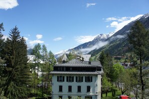 Un bâtiment à deux étages, doté d’un toit en pente, entouré d’arbres et avec des montagnes en arrière-plan.