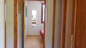 A hallway with wooden doors, a visible window, and a bed in the background.